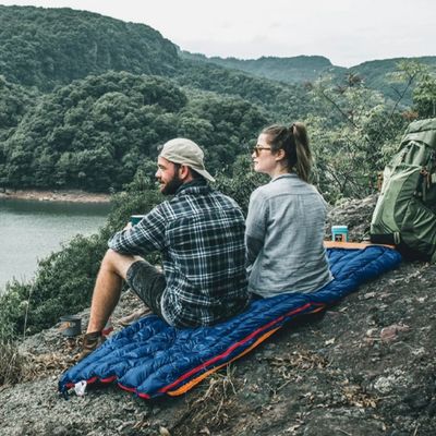 Couple assis rocher sur sac de couchage observe lac