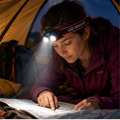 Femme bivouac regarde carte avec lampe frontale rechargeable