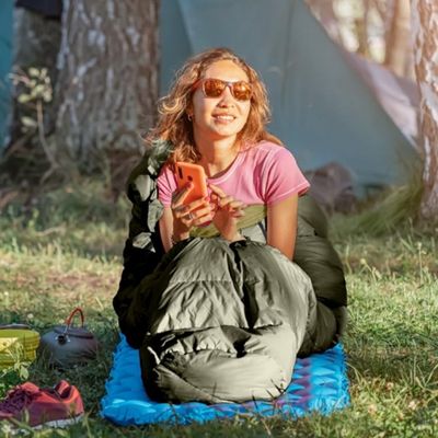 Femme devant tente dans sac de couchage communique portable