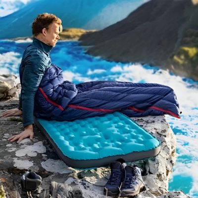 Homme assis sac de couchage rocher surplomb rivière soleil