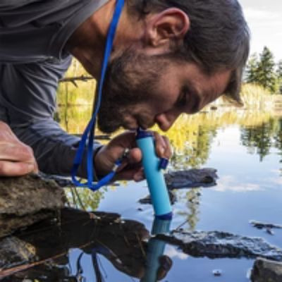 Homme boit directement dans étang avec gourde filtre