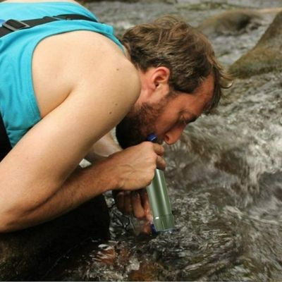 Homme boit paille qui filtre l'eau directement ruisseau