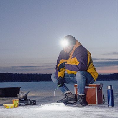 Homme pêche lac gelé avec lampe frontal pour trail