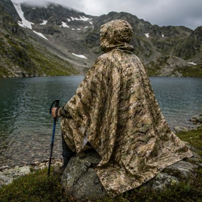 Homme poncho camouflage admire lac assis rocher
