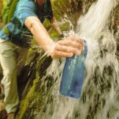 Homme remplit gourde filtrante randonnée sous cascade